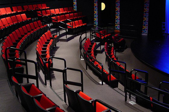 Rows of red theater seats facing a stage in LICM's theater. 