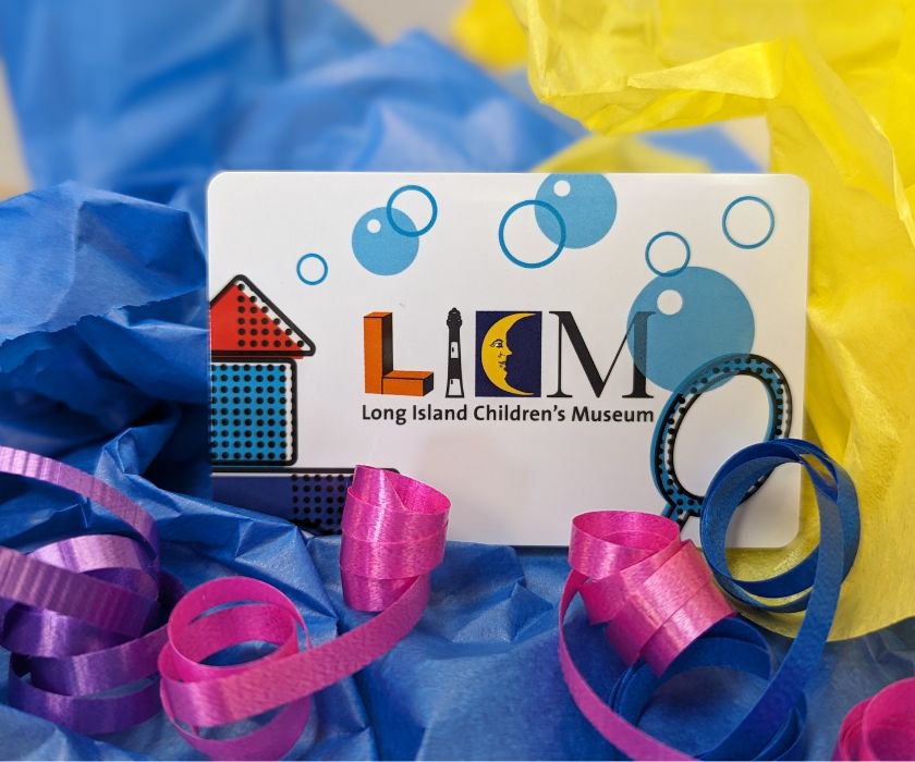 A white giftcard with LICM logo, stacked colorful blocks and blue bubbles against a multi-colored tissue paper background. 