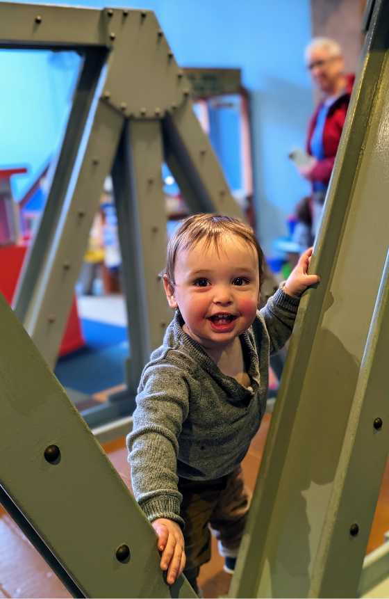 Photograph of a toddler excitingly climbing on an bridge in the tot spot.