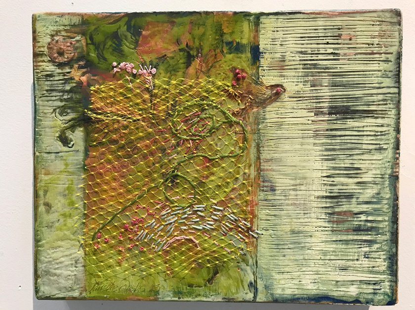 A work of art featuring a mossy piece of wood behind netting, a bird, some flowers, and embroidery.