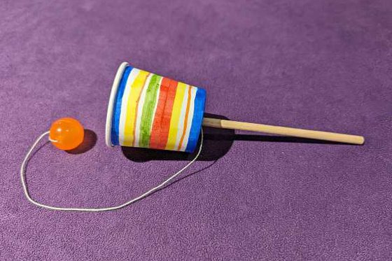 A balero made from a decorated paper cup, a dowel, and a small ball attached to a string. 