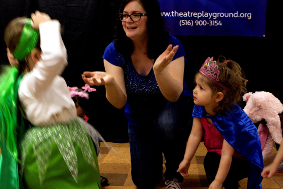 An LICM staff member kneeling on a stage surrounded by children wearing costumes.