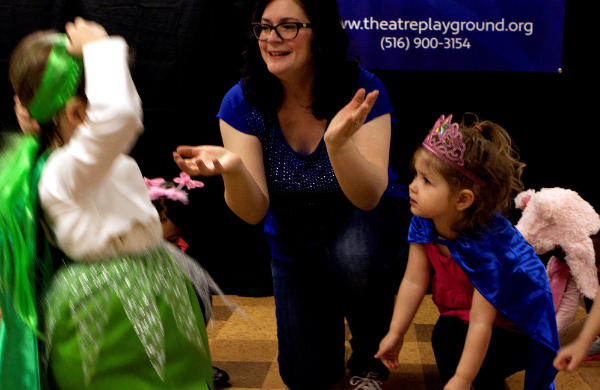 An LICM staff member kneeling on a stage surrounded by children wearing costumes.