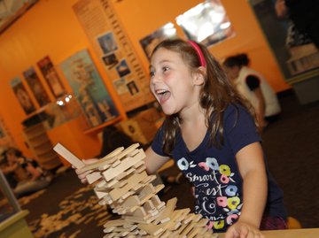 A girl excitedly playing with KEVA blanks and building a structure.