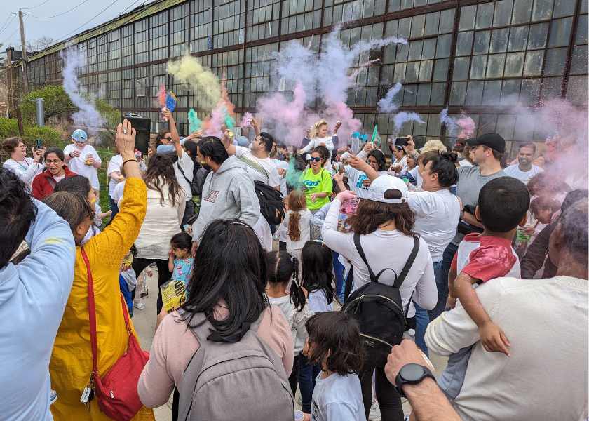 A large group of people outisde the museum doors throwing colorful powder. 