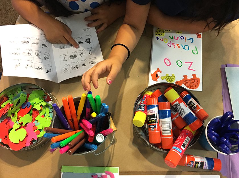 A table with childrens hands reaching for glue sticks and markers while making cards.