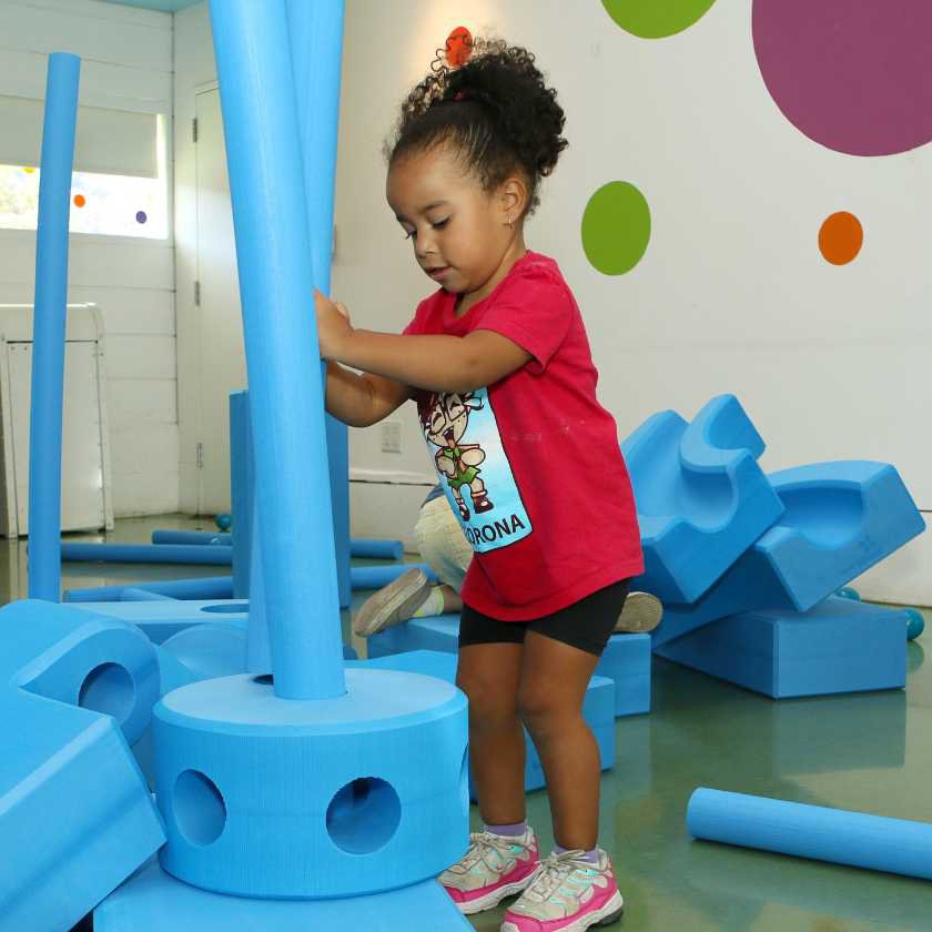 A child surrounded by large foam blocks placing a tubular block inside a circular block. 