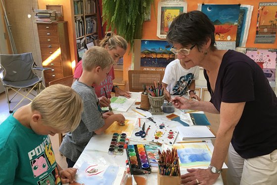 A photograph of an adult helping children complete arts and crafts. 