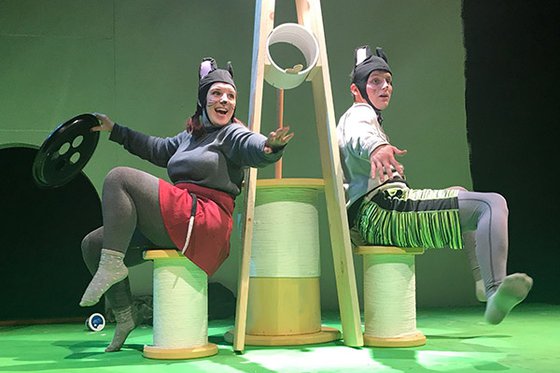 Two actors sitting on stage in between a large clothespin dressed as mice. 