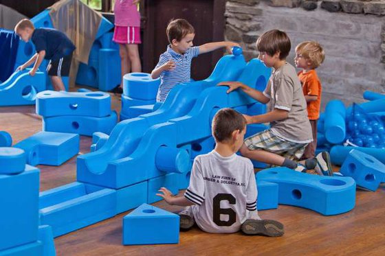 A group of children sitting on the floor playing with large blue foam blocks. 