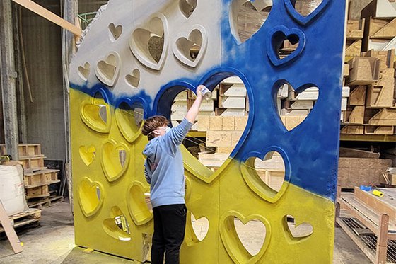 Artist spray painting top portion of a large sculpture blue which features various carved hearts.
