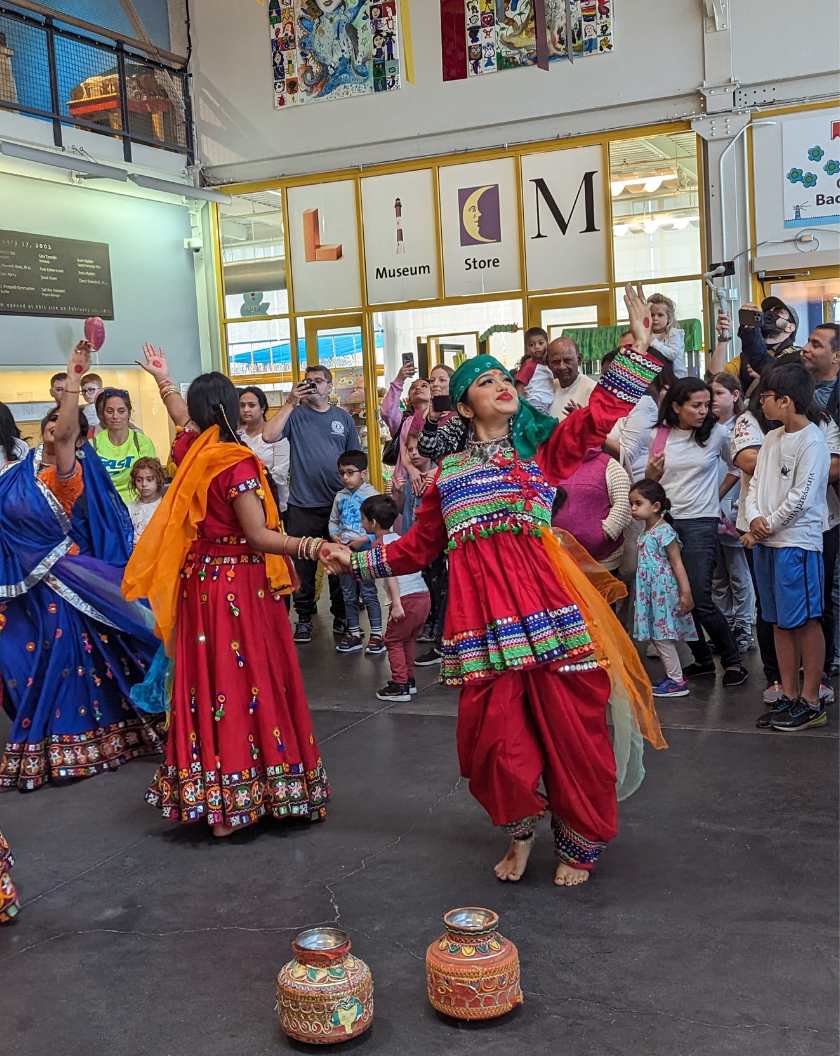 A large group of people watching dancers dressed in traditional Holi attire in LICM's lobby. 