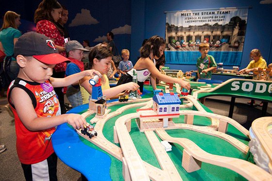 A group of children playing with small trains on train tracks. 