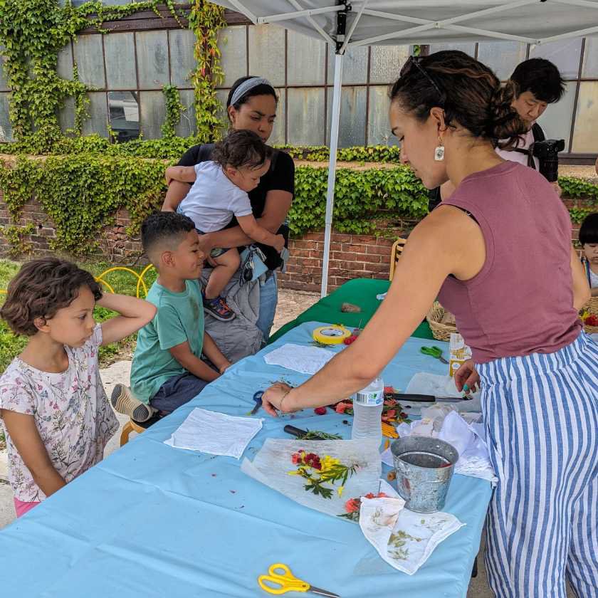 Artist standing at a table with children creating natural dye from palnts. 