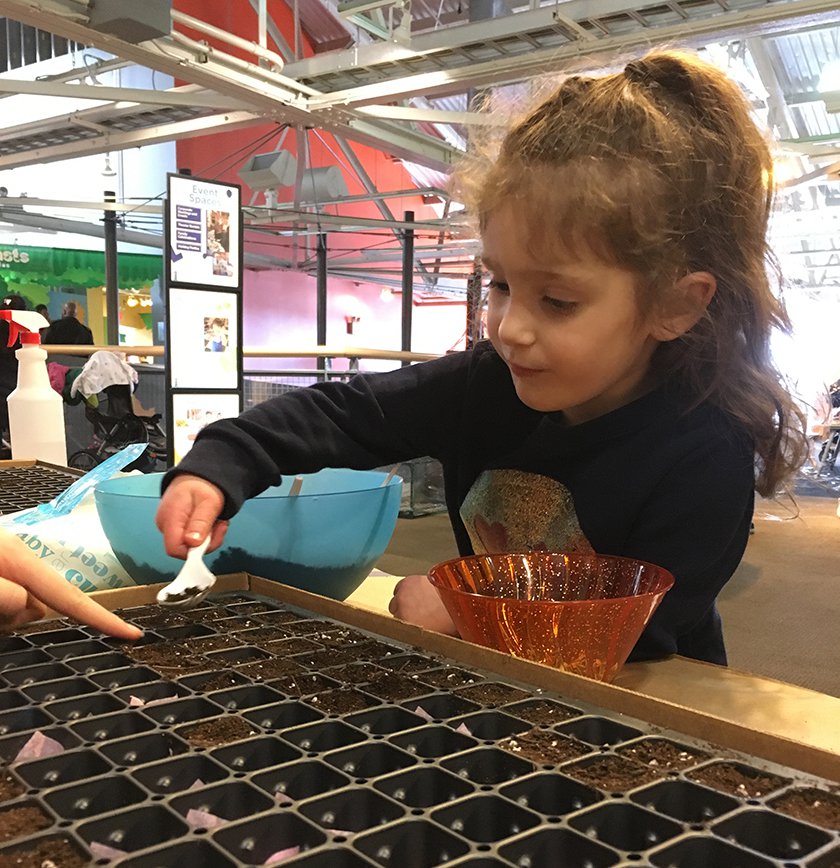 A child using a spoon to transfer dirt from a bowl to mini-planters.