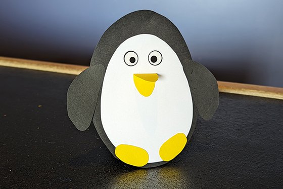 A penguin made from black and white construction paper, with a yellow beak and feet. 