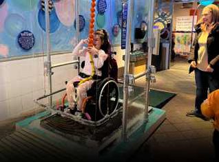 A child in a wheelchair on a platform and pulling the bubble around her using a rope. 