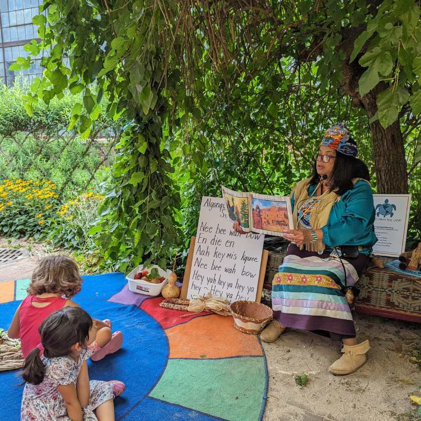 Artist Silva Dennis reading children a book about indigenous people while dressed in traditional indigenous attire. 