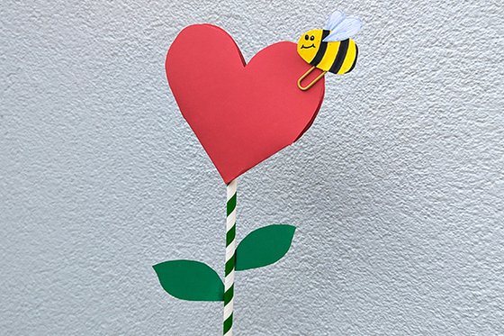 Flower made from red heart with bumble bee and stem made from green and white straw.